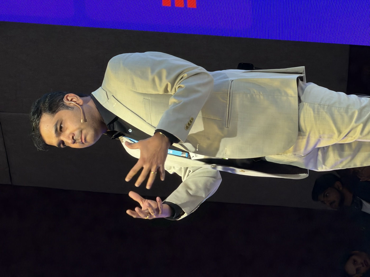Ameet Deshpande speaking on stage in a light suit